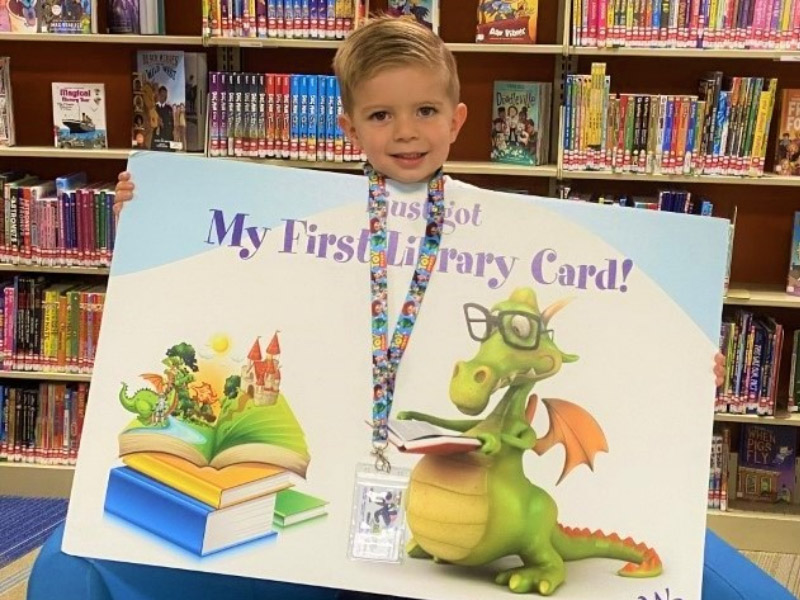 kid holding sigh that says "first library card"